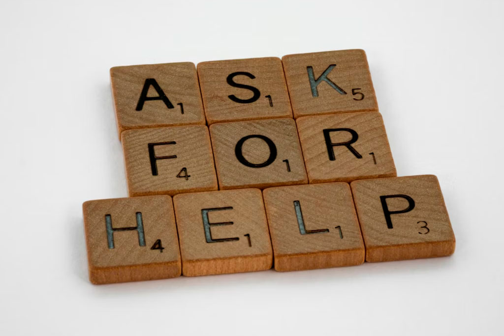 Fichas de juego Scrabble formando la frase Ask for Help, representando la necesidad de ayuda experta en soporte de hosting.